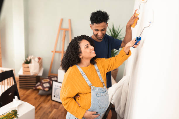 Happy multiracial couple expecting a baby and painting walls at their new home